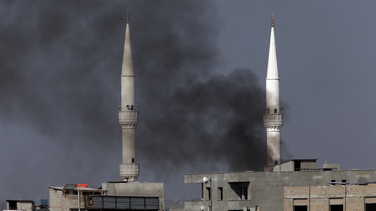 Spoza minaretov mešity stýpa dym po bombardovaní Sýrie tureckými vojskami.