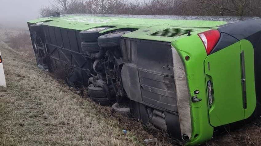 Prevrátený autobus skončil mimo cesty.