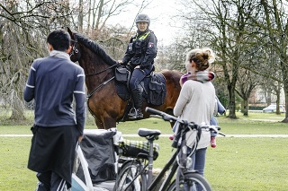 Policajtka na koni upozorňuje mladú dvojicu, že v rámci opatrení je zakázané sedieť na lavičkách.