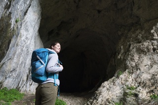 Woman explorer staning in front of the cave in the mountains