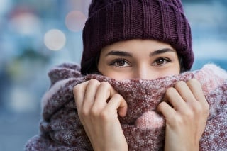 Winter portrait of young beautiful woman covering face with woolen scarf. Closeup of happy girl feeling cold outdoor in the city. Young woman holding scarf and looking at camera.'r