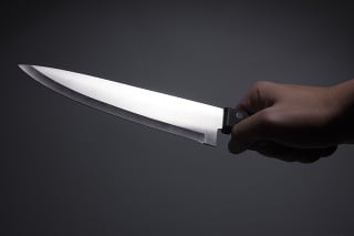 Male hand holding large, sharp, shiny kitchen knife. Isolated on dark background. Photo is taken with dslr camera indoors.