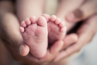 Feet of a newborn baby in the hands of parents. Happy Family oncept. Mum and Dad hug their baby's legs.