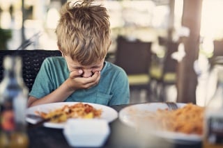 Little boy fussy eater in restaurant. The boy doesnt want to eat and he is even going to throw up even looking at his plate.
