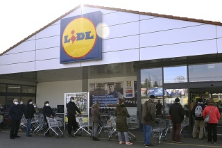 Zákazníci s ochrannými rúškami stoja v rade pred predajňou  v Trenčíne. 