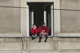 Pár znudene sedí na parapete v otvorenom okne vo Varšave počas pandémie koronavírusu.