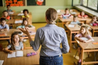 Back view of a female teacher teaching large group of elementary students in the classroom.