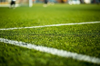 Close-up of artificial turf. Blurred legs of soccer players in the background.