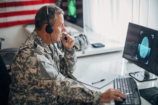 One mature man, American soldier sitting in headquarters office alone, using computer.