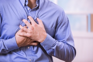 Mid-adult man clutching his chest in pain with a possible heart attack.  He wears a blue, button down dress shirt.  Heart disease.