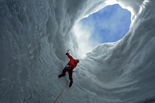 Man climbing glacier with ice pick