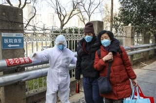 Zdravotník v ochrannom odeve pomáha páru pred nemocnicou v meste Wu-chan.