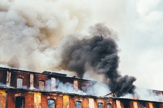 Grey clouds of smoke swirling out of an old abandoned industrial building. 