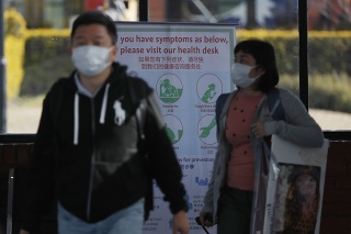 Cestujúci s rúškami na medzinárodnom letisku v Káthmandu, v pozadí informačná tabula o koronavíruse.