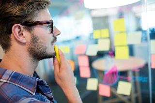 Thoughtful man reading sticky notes on the glass wall in office