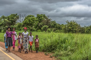 Malange / Angola - 12 08 2018: View of a group at young girls walking along roadside, tropical landscape as background