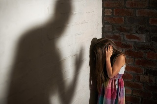 Abused little girl huddled over while the shadow of her abuser looms towards her