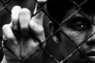 Depressed man standing behind a fence, hand grabs steel mesh cage,close up on face in white tone, abuse concept