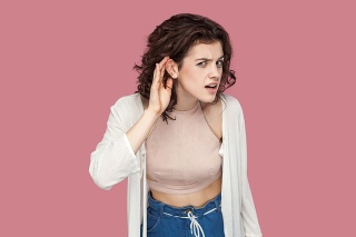 what? tell me louder. Portrait of attentive brunette young woman with curly hairstyle in casual style standing with hand gesture on ear and looking at camera. studio shot isolated on pink background.