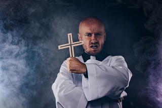 Catholic priest exorcist in white surplice and black shirt with cleric collar praying with crucifix