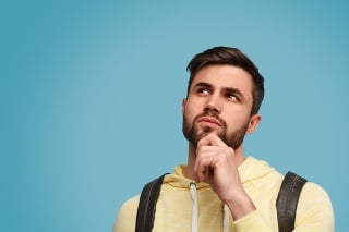 Handsome bearded guy with backpack looking up in doubts on studies against blue background