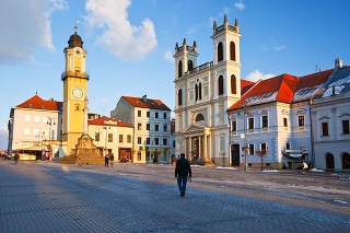 Banska Bystrica, Slovakia – January 16, 2016: Lonly walker in the main square in Banska Bystrica, central Slovakia. Image shows the cathedral, plague column and clock tower.