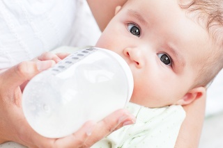 Close-up of a baby drinking milk in his mother's arms at home