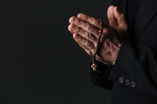 Hands of priest holding rosary and praying over black background
