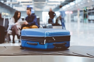 Blue suitcase on conveyor at baggage claim line terminal of the international airport. People in the background.