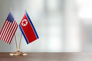 American and North Korean flag pair on desk over defocused background. Horizontal composition with copy space and selective focus.