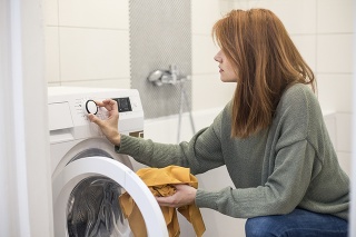 Young woman doing laundry, setting a washing machine. About 25 years old, Caucasian female.