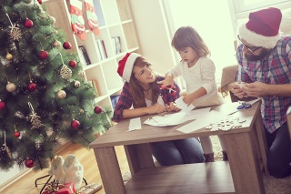 Mother, father and daughter sitting on a living room floor, cutting paper snowflakes and enjoying winter holidays together. Focus on the mother