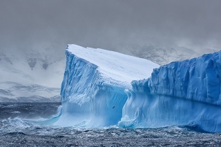 Massive Iceberg floating in the Southern Ocean in Antarctica with snow covered mountains in the background