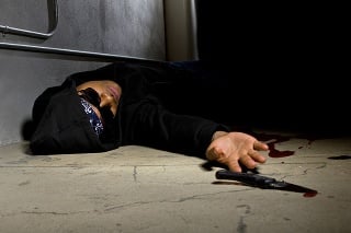 Photo of a man in a street alley killed with a knife.  The foreground has a knife with blood which is probably the murder weapon.  The set looks like a crime scene.  The man is laying on the ground dying.  The image depics gang violence.  This version has blood.
