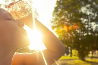 Woman using water bottle to cool down. Fitness and wellbeing concept with female athlete cooling down on a city street. She is holding a water bottle to her head to cool down. The sun is low creating long shadows and some lens flare. Copy space