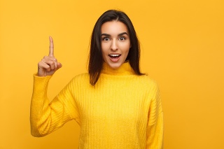 Casual young brunette in yellow sweater holding finger up enlightened with new thought looking shocked.
