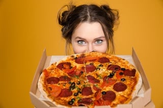 Lovely cute positive young woman hiding behind pizza over yellow background