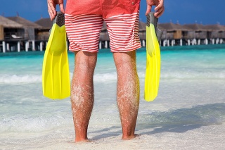 Man with fins in his hands standing on a Maldivian beach and watching the scenery