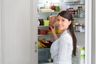 Woman at home opening the fridge and taking food out while looking at the camera smiling