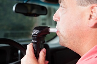 A male driver is blowing into an ignition interlock system which checks his alcohol concentration before allowing the vehicle to be started. Ignition interlock devices may be an alternative sentence for drunk driving or a probation requirement for those who have received a DUI.