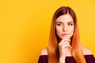 Portrait of red straight-haired attractive cute nice curious young girl, hand touching chin, thoughtful. Copy space. Isolated over bright vivid yellow background