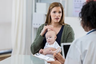 Worried Caucasian mother describes her baby girl's symptoms to an attentive pediatrician.The mother is pointing to a spot on the baby's head.