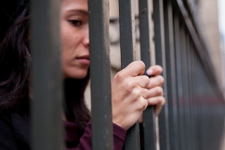 Close up of a female prisoner behind bars. Stress and anxiety showing on her face. Focus on her hands.