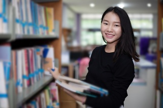 Asian female students holding for selection Book  in library
