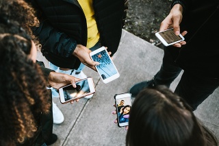 A young adults all viewing something on their smart phones.   Mixed ethnic group.  Horizontal image, as viewed from above.  Faces not visible.