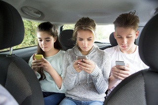 Three teenagers text messaging in the back of a car