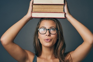 Studio shot of a young woman holding a pile of books against a grey background