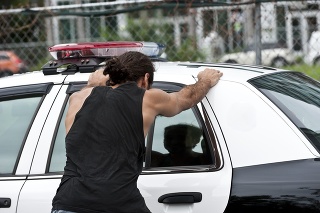 Hispanic man with his hands on top of a police car from behind