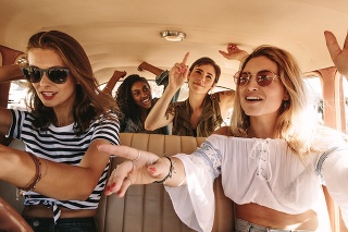 Group of young women singing and dancing in the car on a road trip. Multiracial female friends having fun on a car ride.