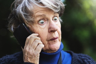 A senior woman listening to her mobile phone outdoors looks utterly horrified and shocked by what she hears.